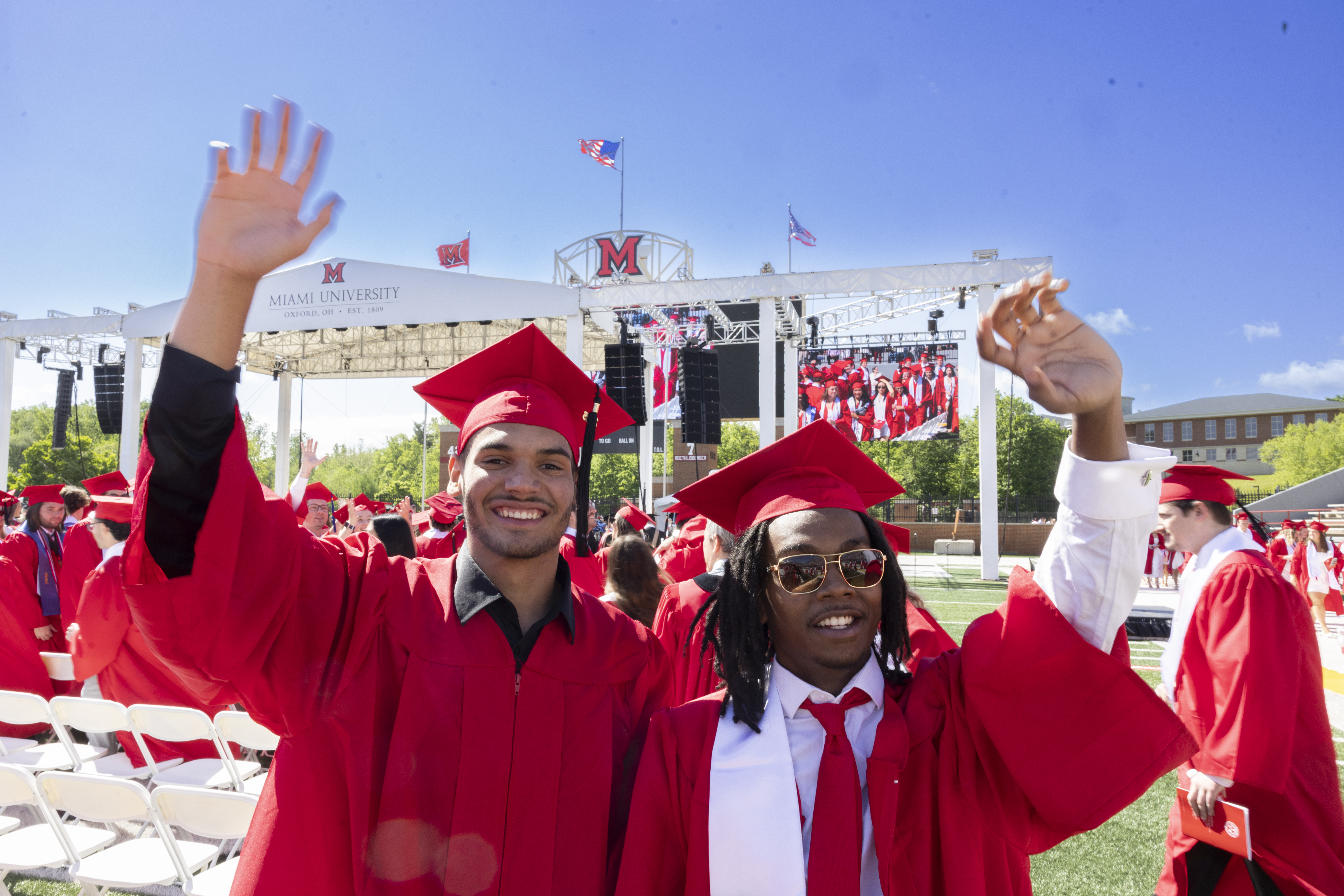 Two Miami University students wave to the crowd during commencement.
