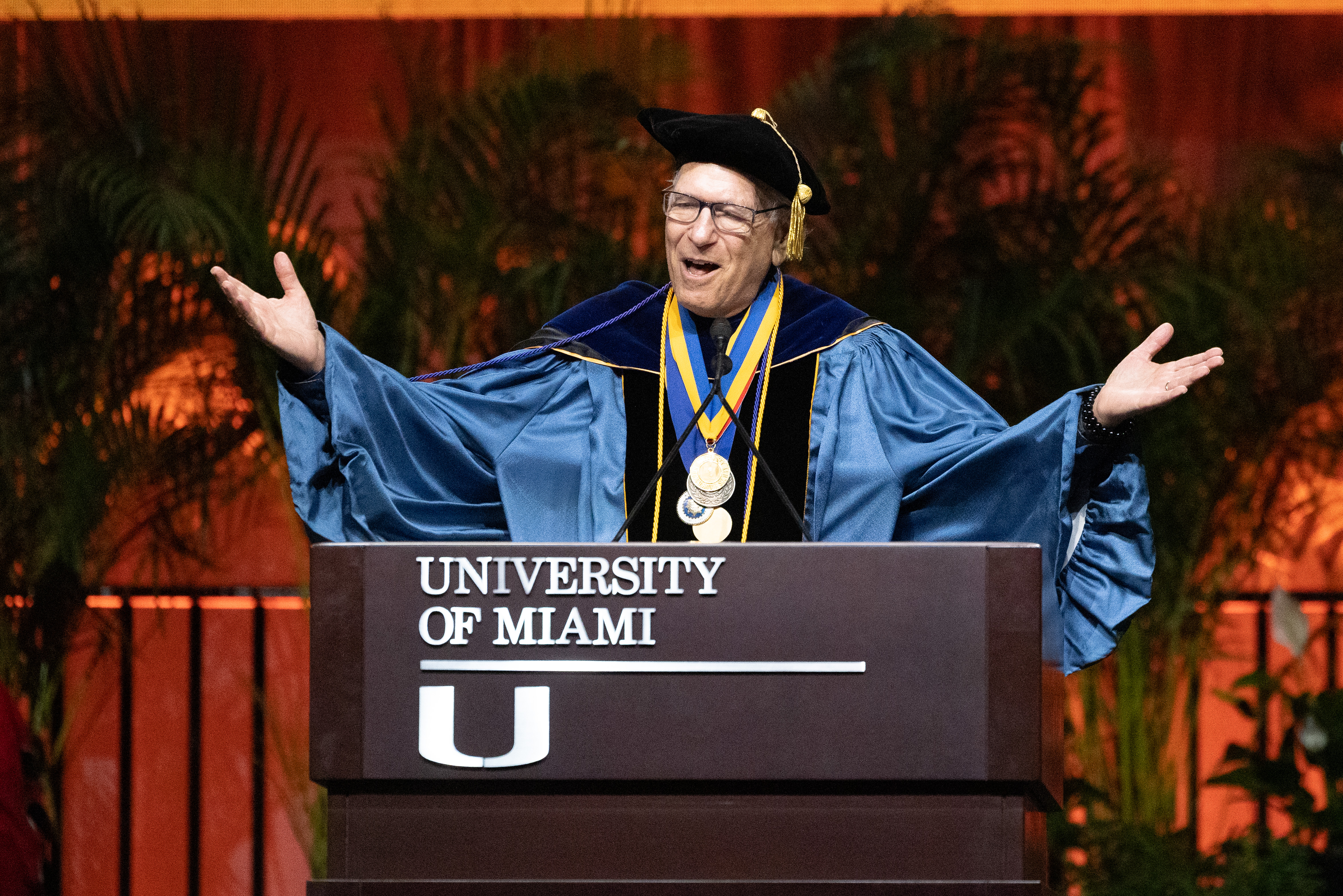 Man in graduation gown speaks at podium with