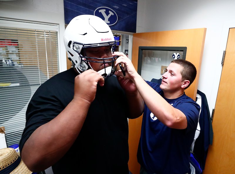 Mo Langi tries on a helmet with help from Assistant Equipment Manger Billy Nixon. Photo by Jaren Wilkey/BYU