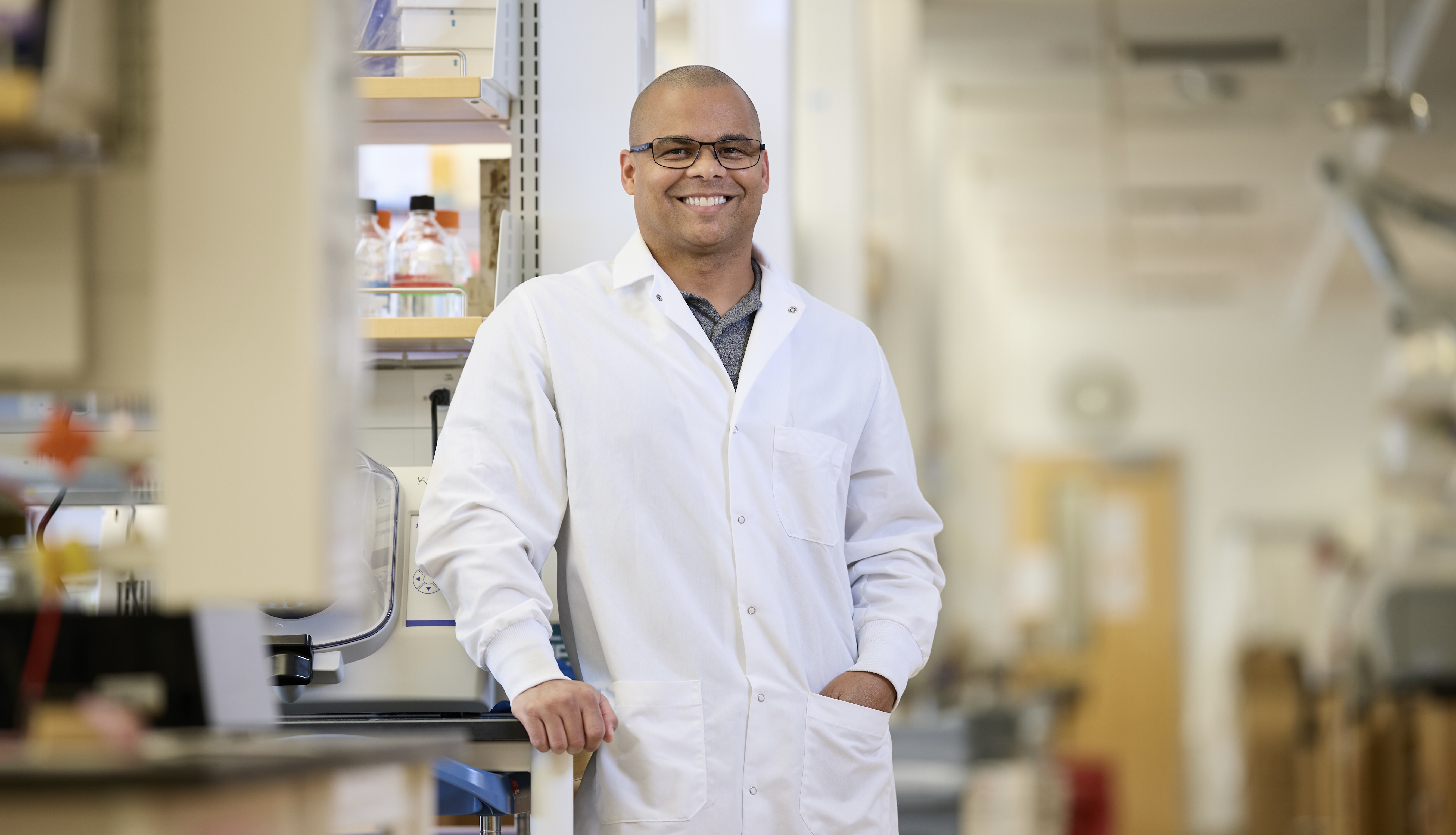 Smiling researcher in lab coat stands in a bright laboratory. He wears ...