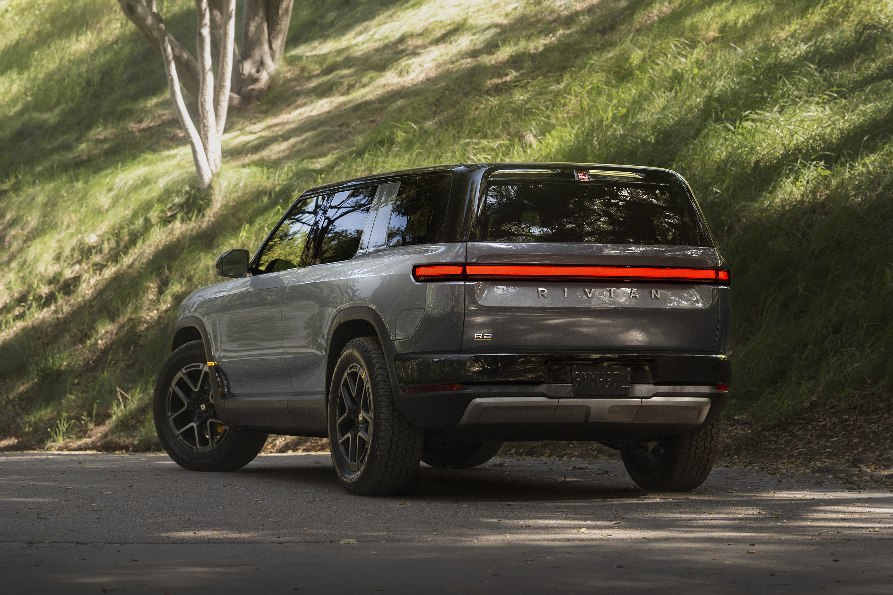 Rear view of the gray Rivian R2 SUV parked on a paved road. A ...