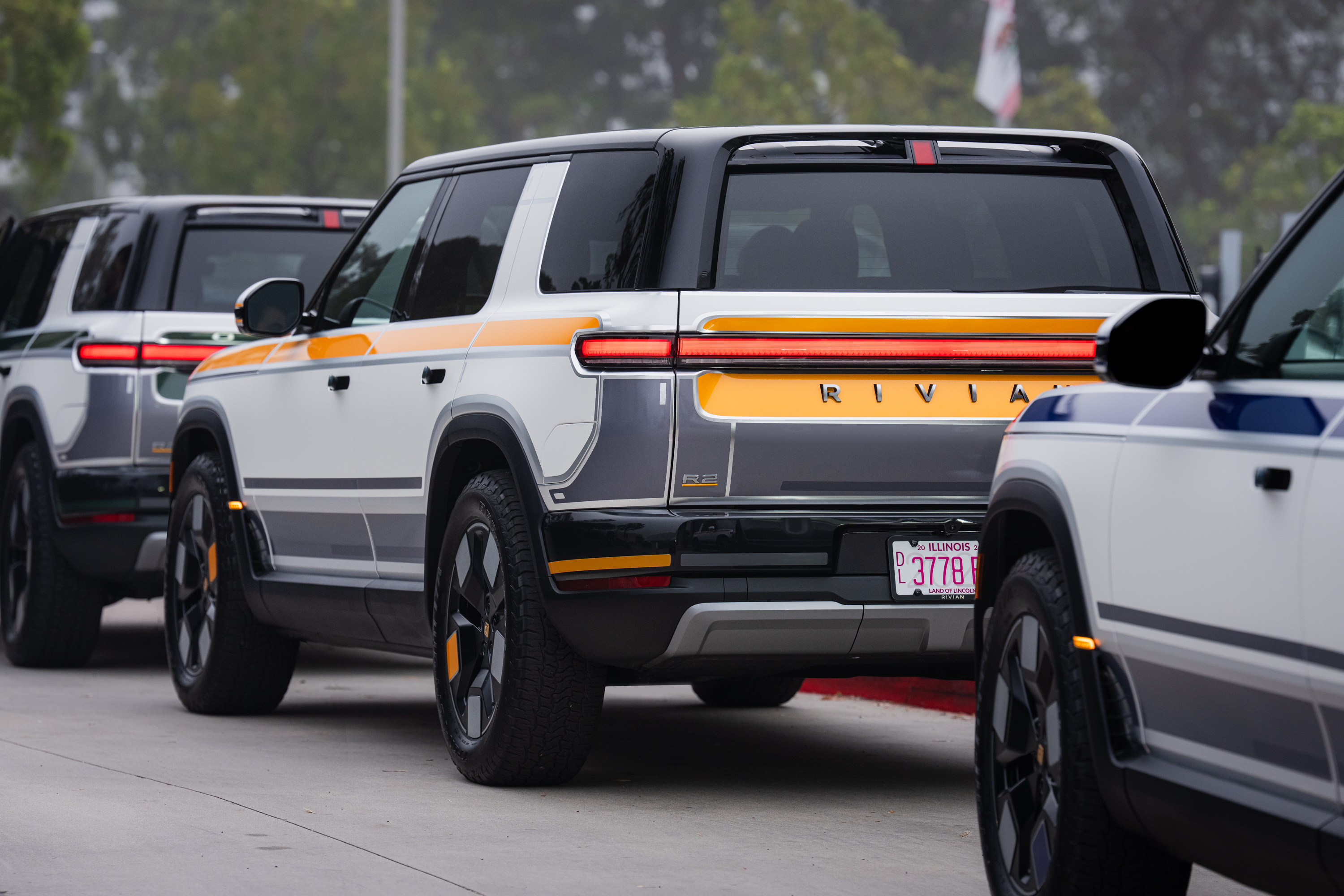 Rear view of a white and gray Rivian R2 SUV with orange accents, parked ...