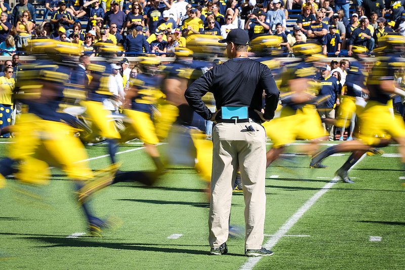 Coach Harbaugh watches the players run across the field during warmups.