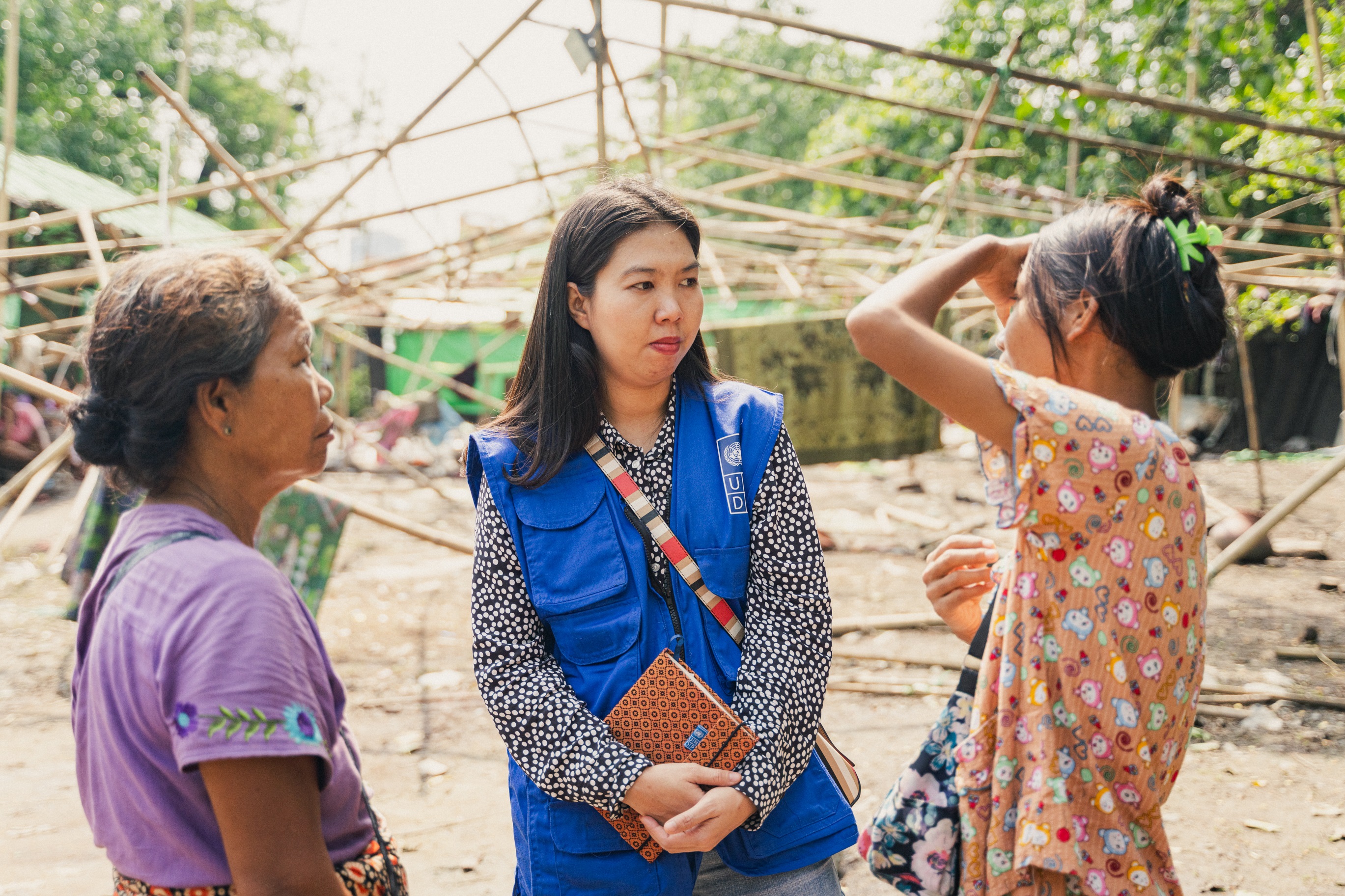 Woman in blue vest speaks with two other women. Behind them is a ...