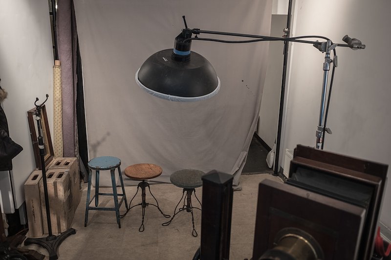 A very simple portrait studio, a few stools, a back drop, and a single overhead lamp.