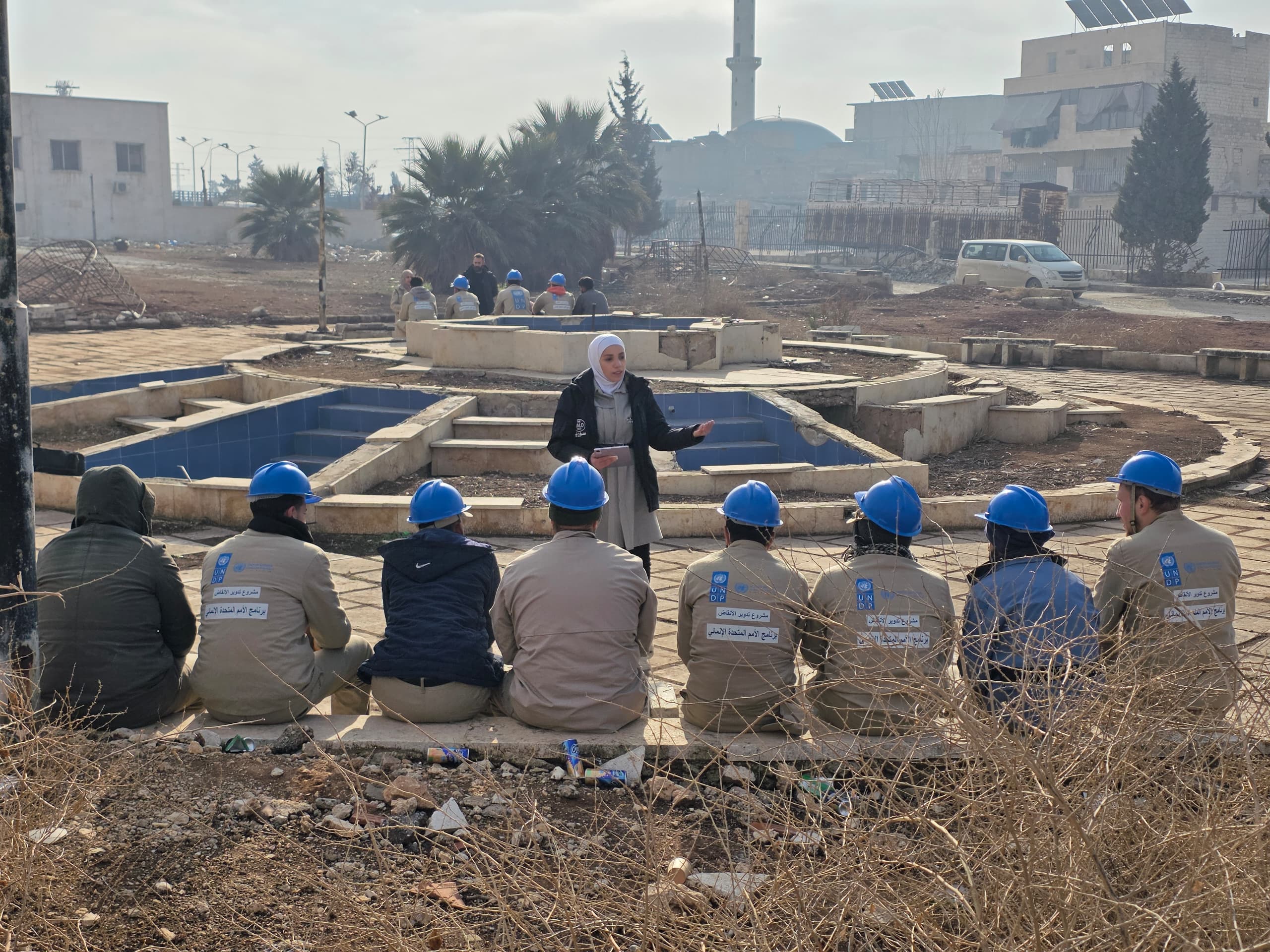A woman gestures while speaking to workers in blue hard hats seated in ...