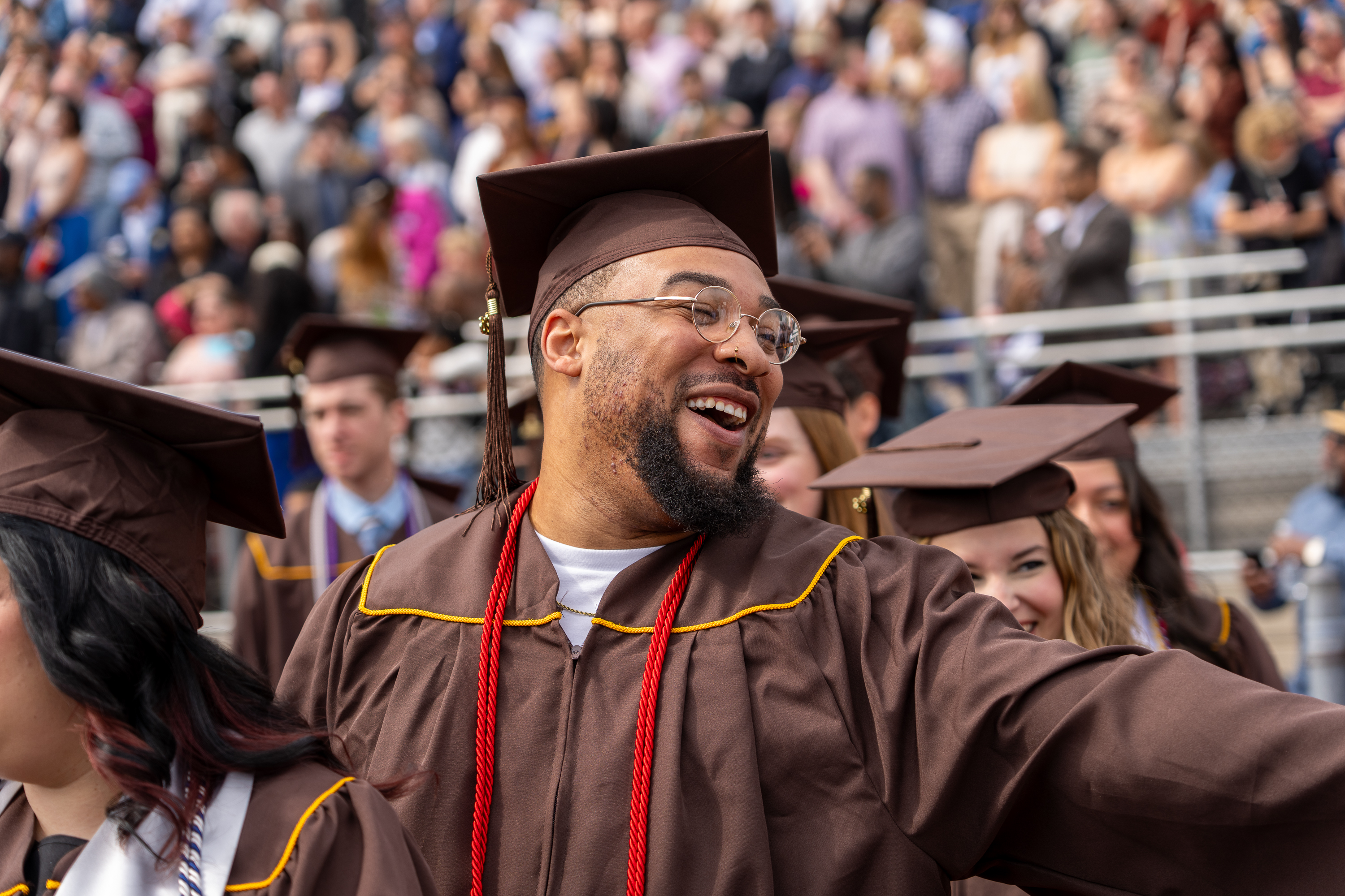 Smiling graduate in cap and gown stands among peers at outdoor ...