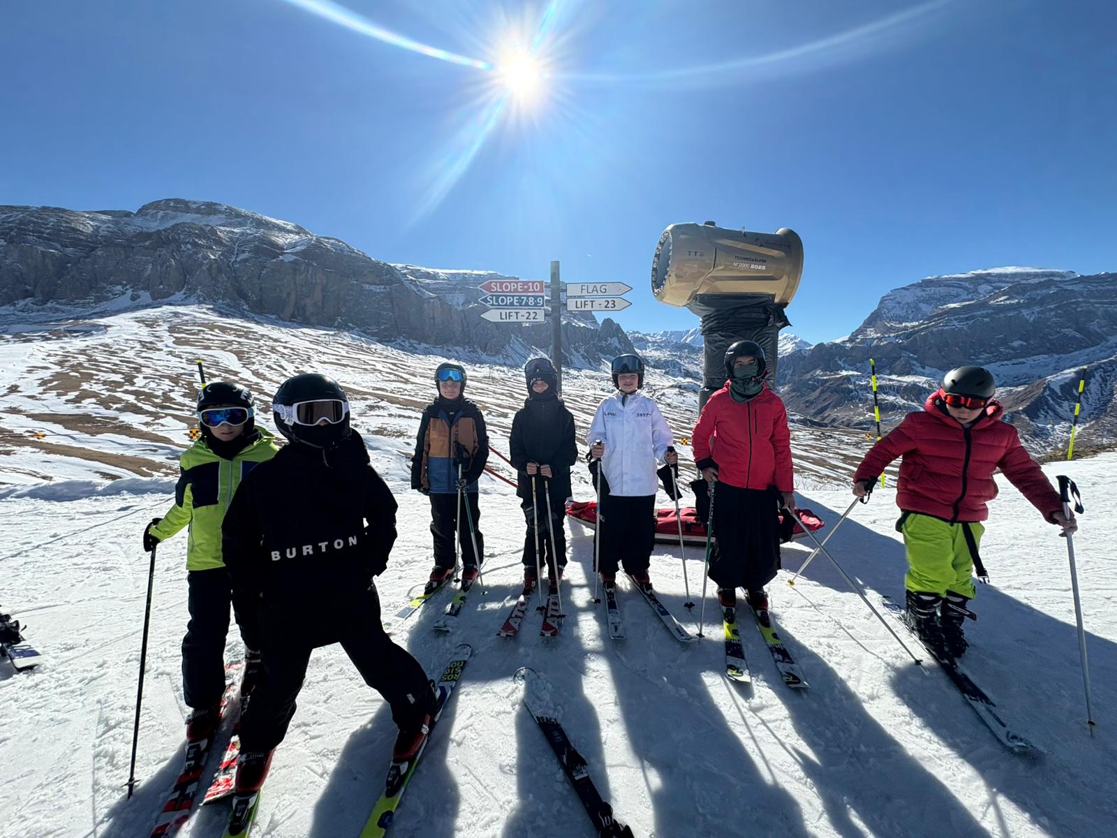 A group of young skiers stand on a snowy slope under a bright sun in ...