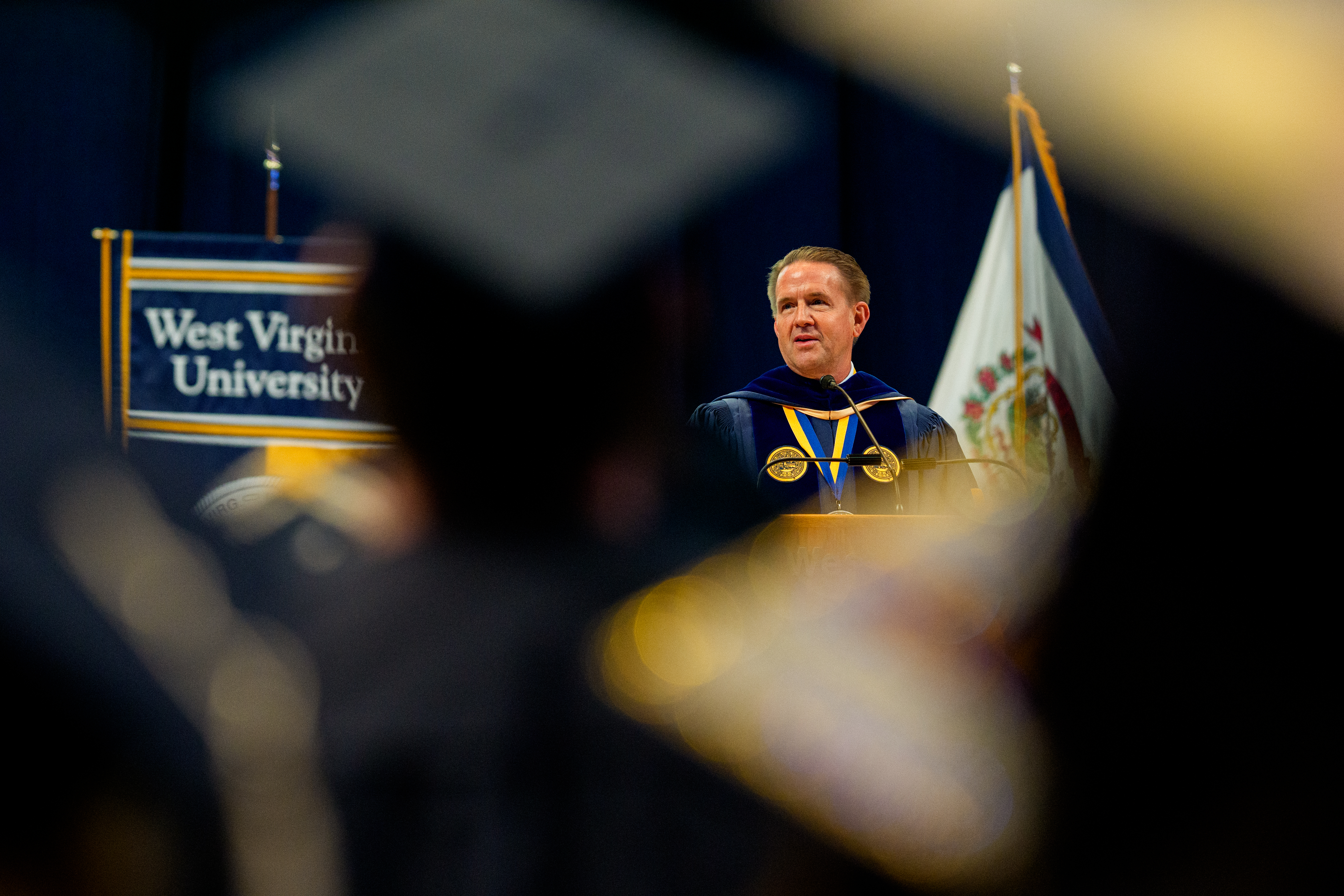 Man in graduation regalia speaks at podium during College of Creative ...