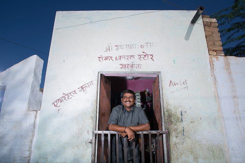 Sankarlal leaning over the balcony of his shop, smiling.