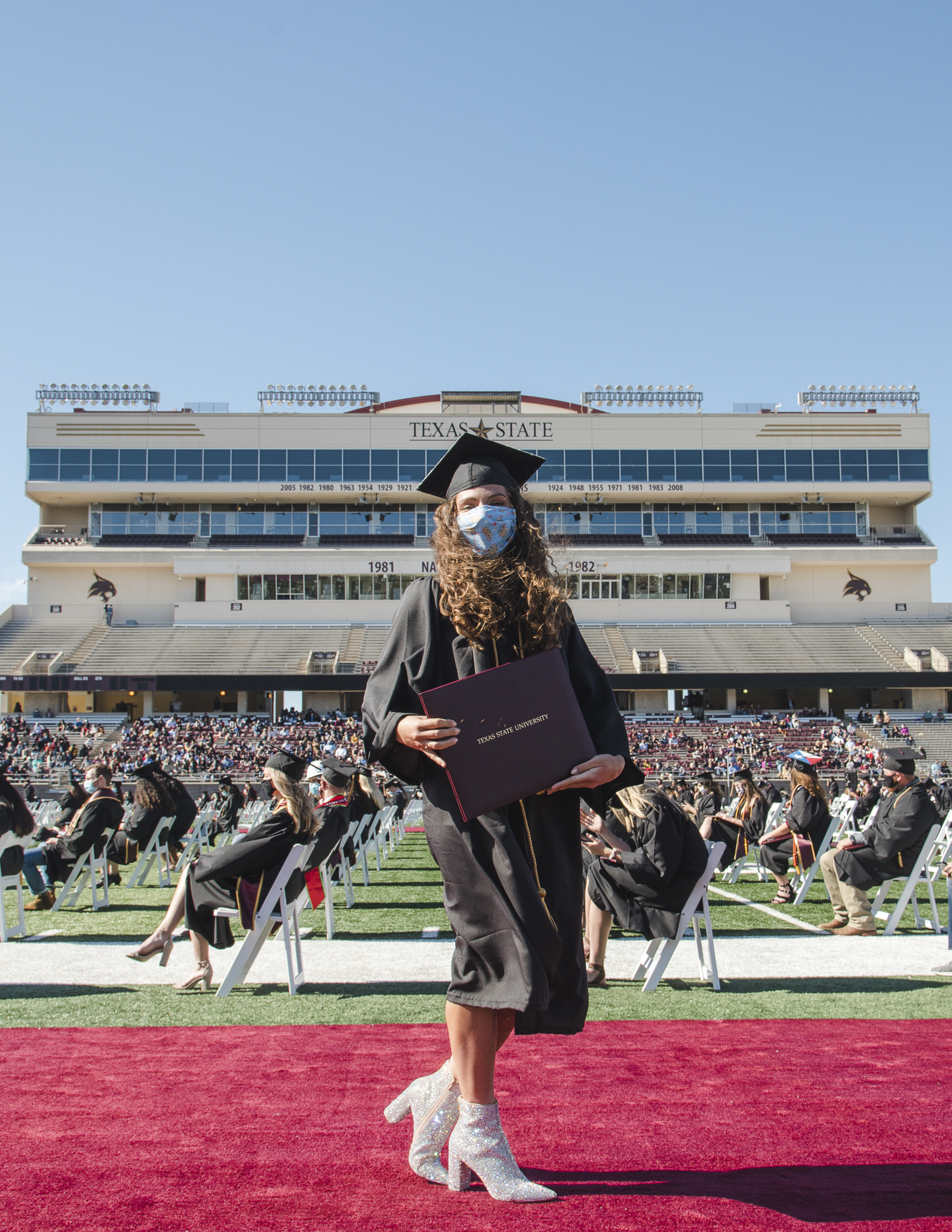 A TXST graduate poses for a photo during commencement on a sunny day.