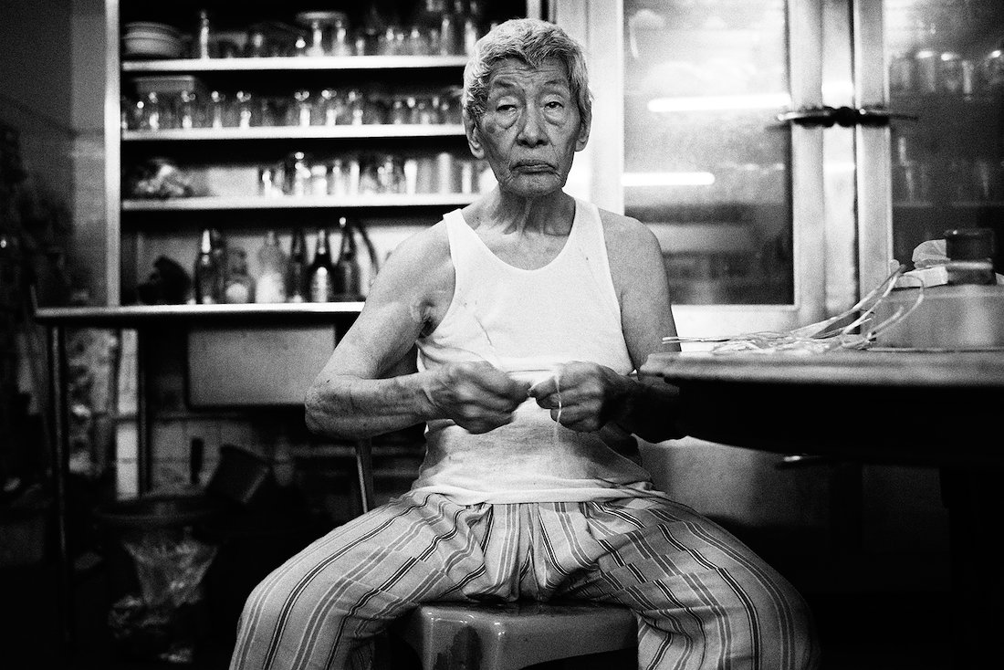 elder shi tying raffia strings to be used with take away coffee 'cups' - which are empty sweetened milk cans