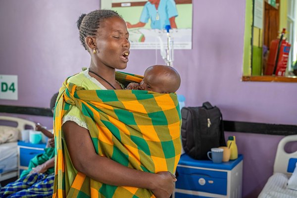 A mum prays while holding her son during ward devotions.