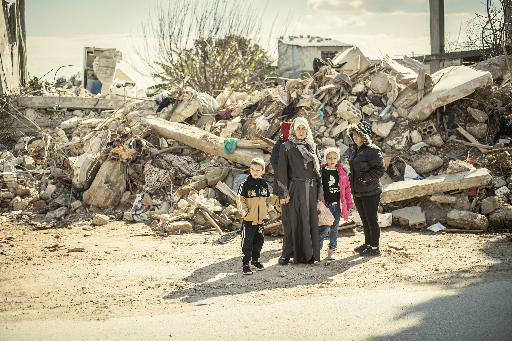 A woman in a hijab stands holding hands with a boy and girl in front of ...