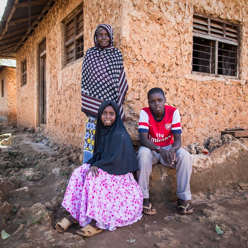Rehema sitting outside her house with her brother Mohammed and mother Makasi.