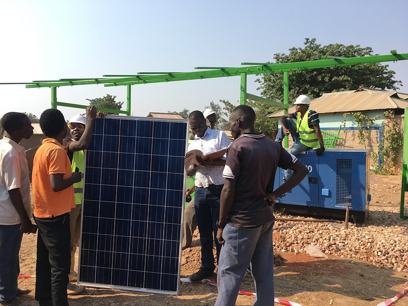 SEI researcher Mbeo Ogeya takes notes while PowerGen workers install the solar mini-grid