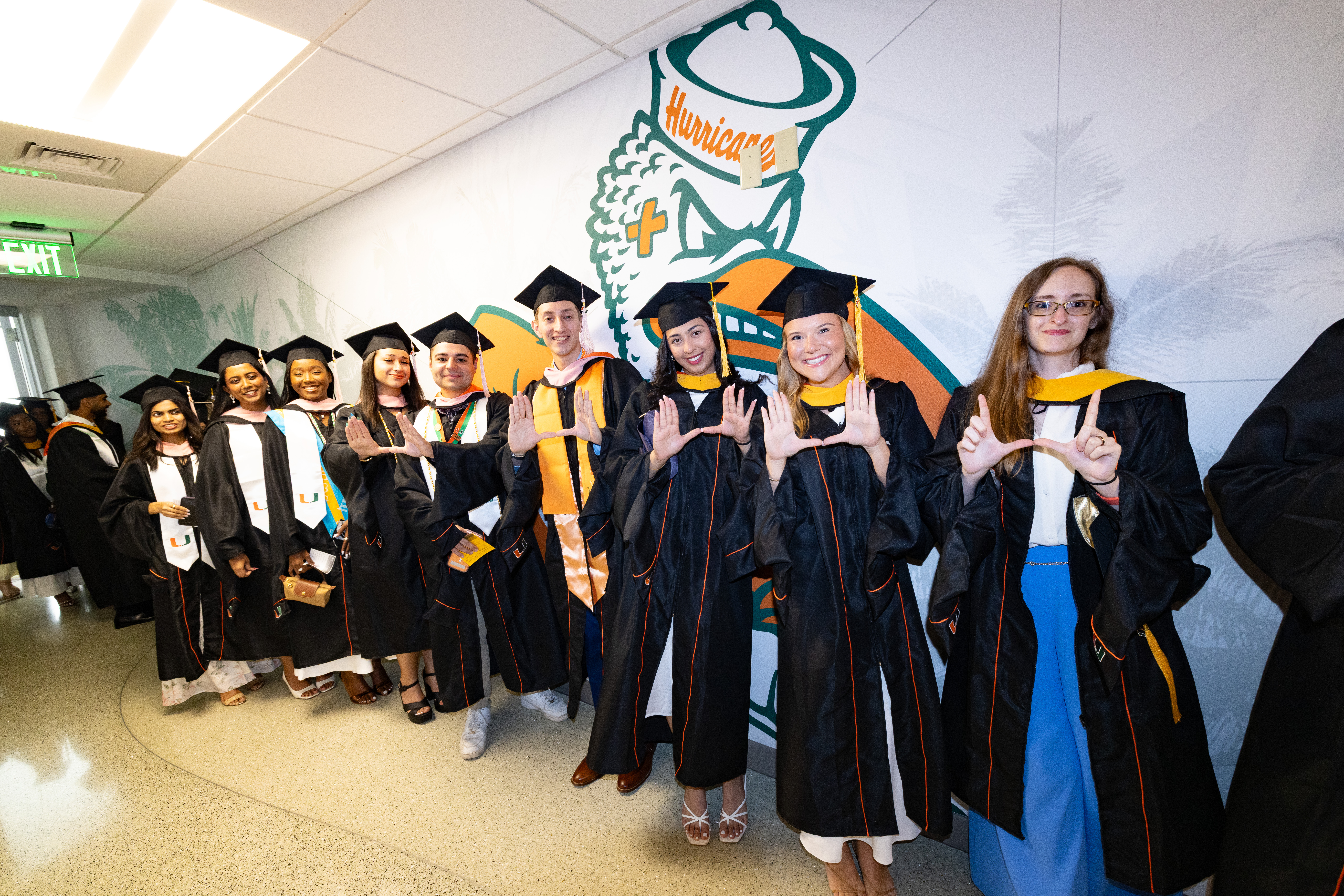 Graduates in black gowns pose in a line with the