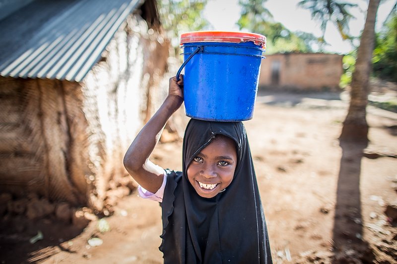 Rehema carrying a pail of water on her head.