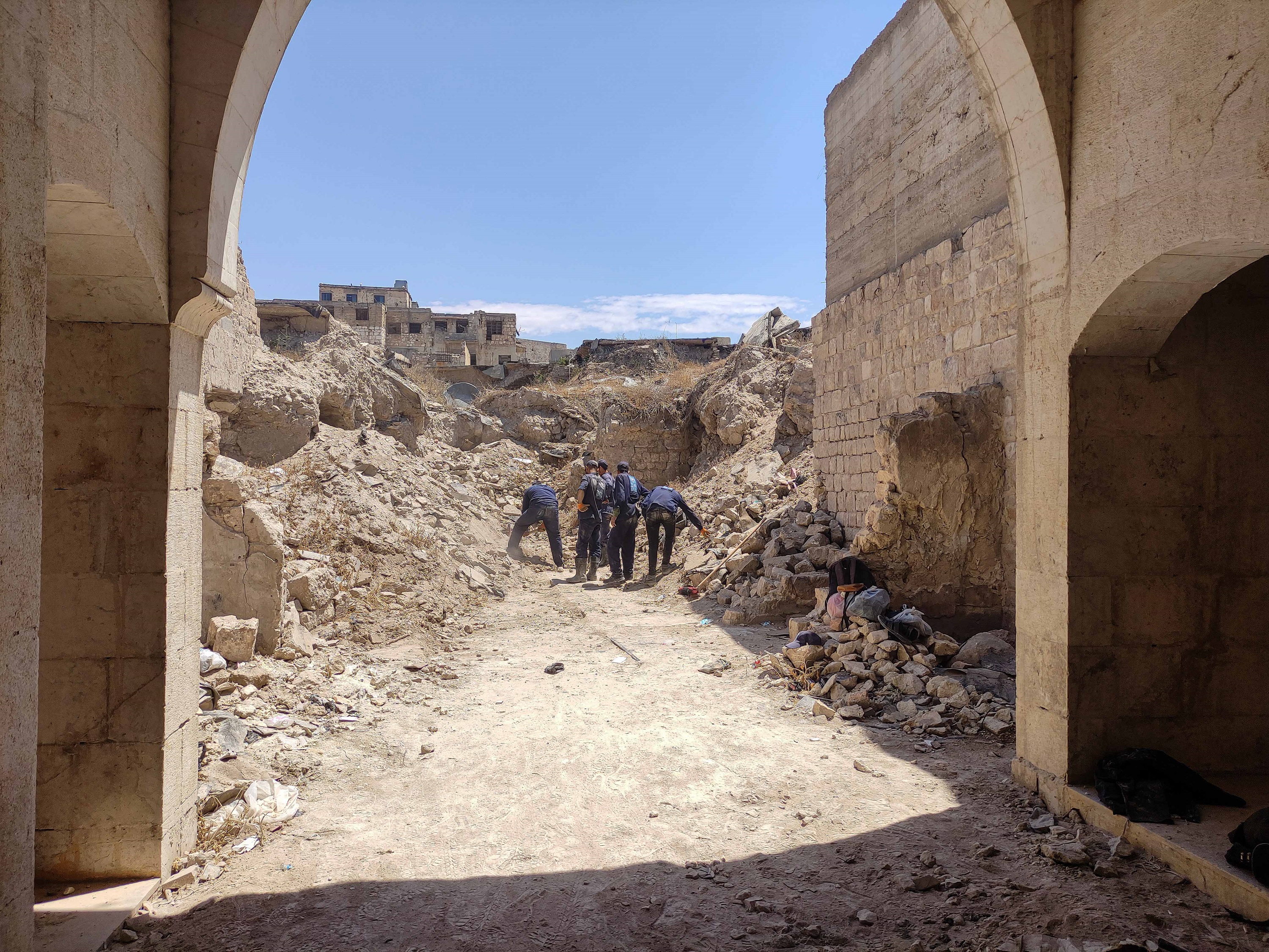 Workers clear rubble in Aleppo, seen through a stone archway. Debris ...