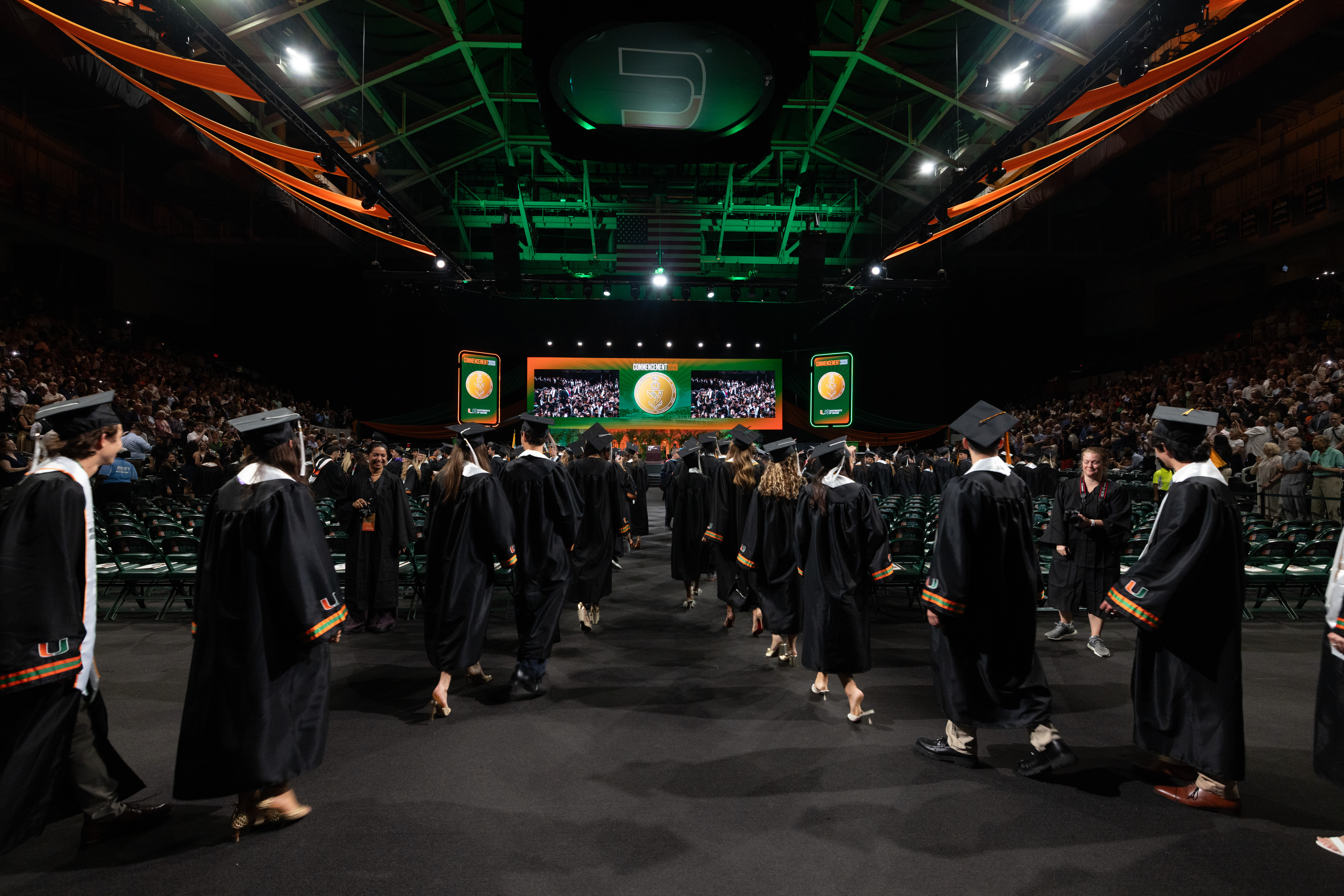 Graduates in black gowns walk down the aisle during the Spring 2026 ...