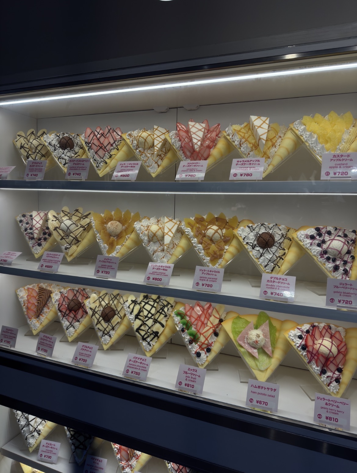 A display case shows rows of triangular crepes with various sweet and ...