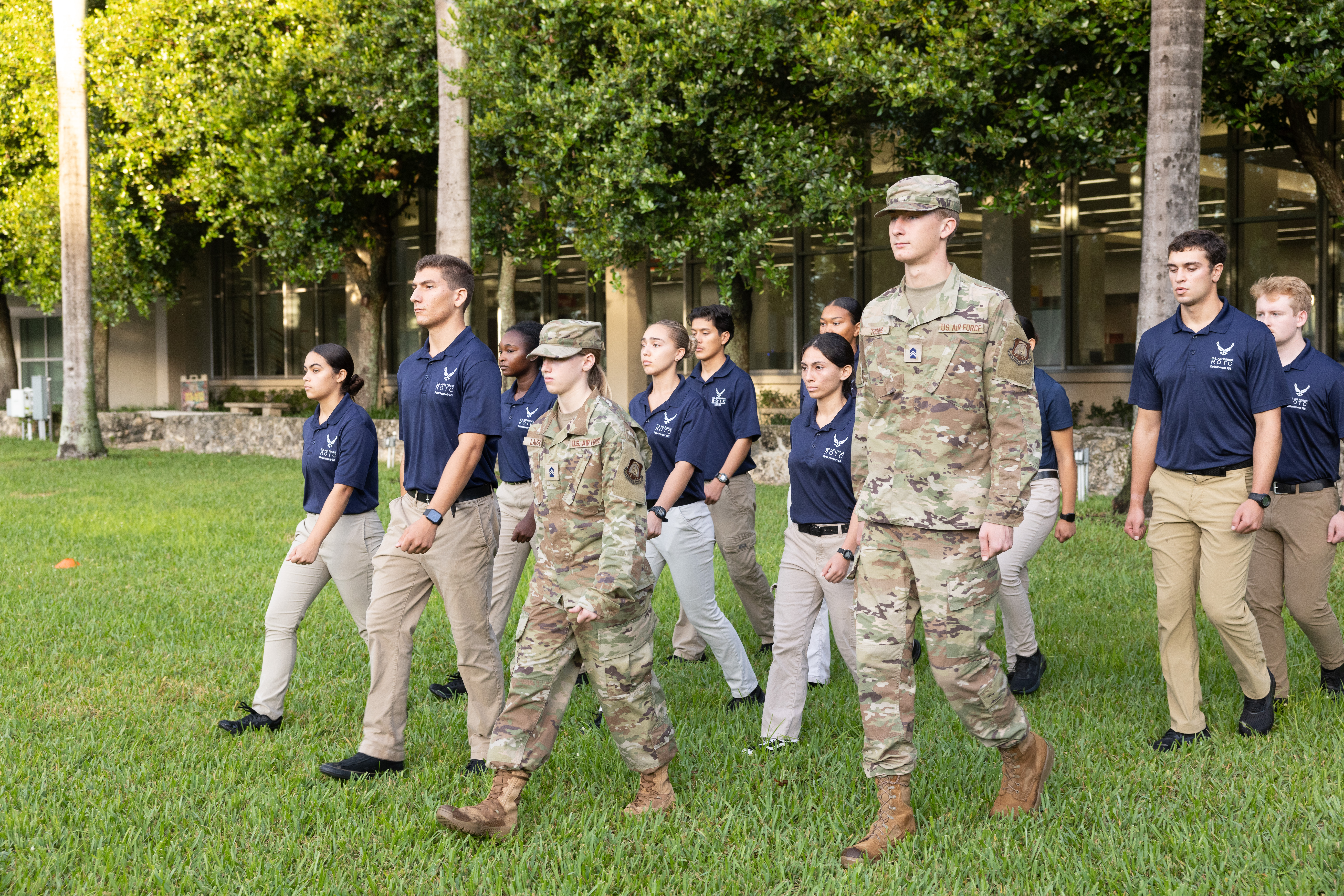 A group of ROTC cadets march on a grassy field. Some wear military ...