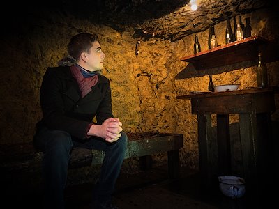 A student sits in the cave surrounded by items left from the war.