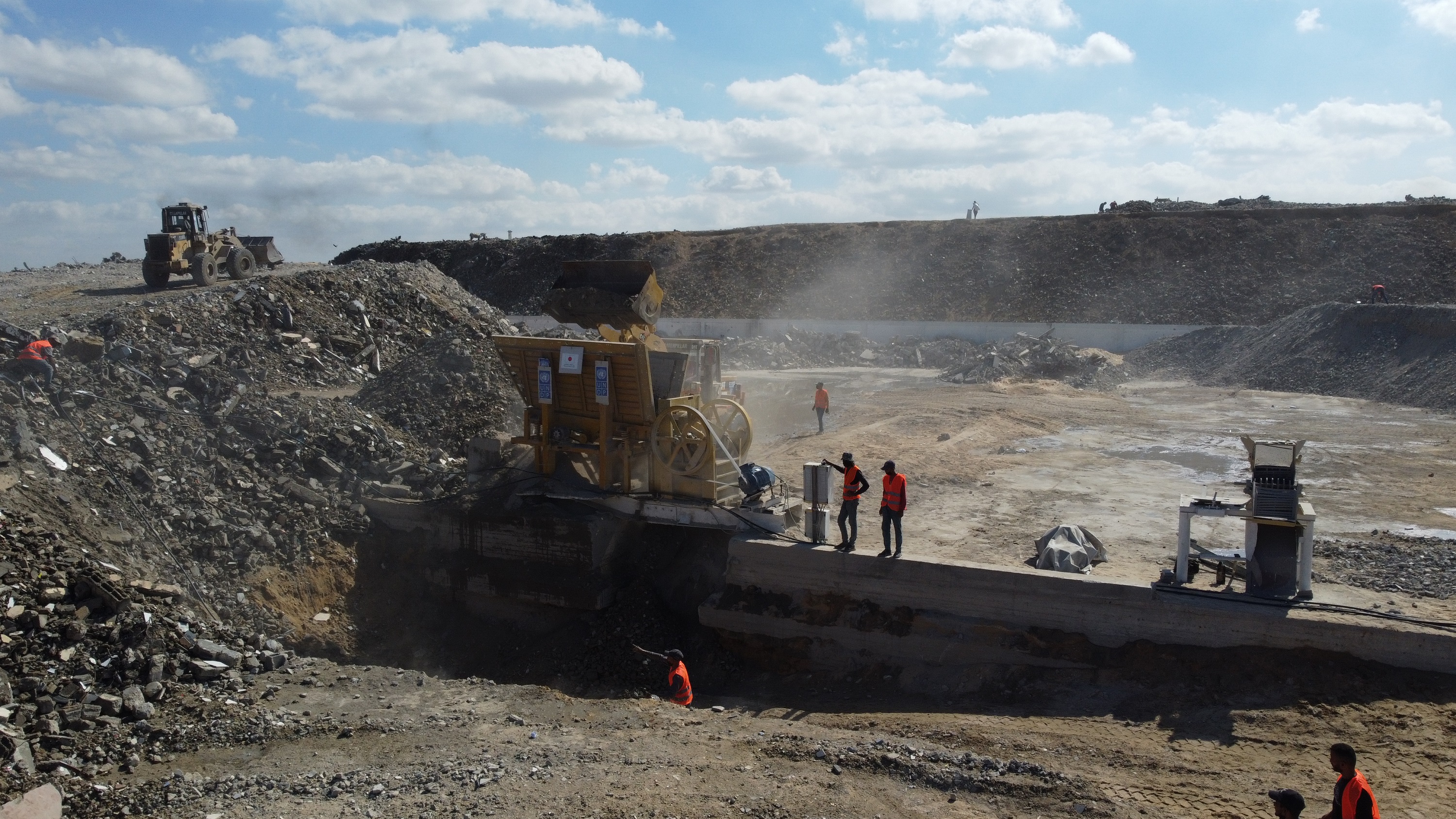 Construction site shows workers near heavy machinery, including a rock ...