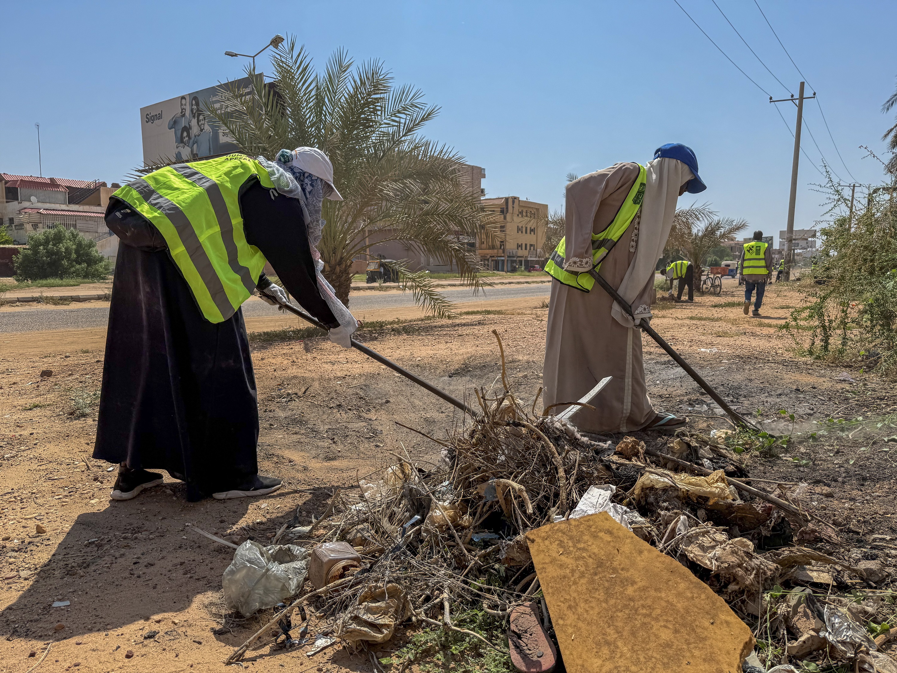 Two women wearing long dresses and safety vests clean up trash with ...