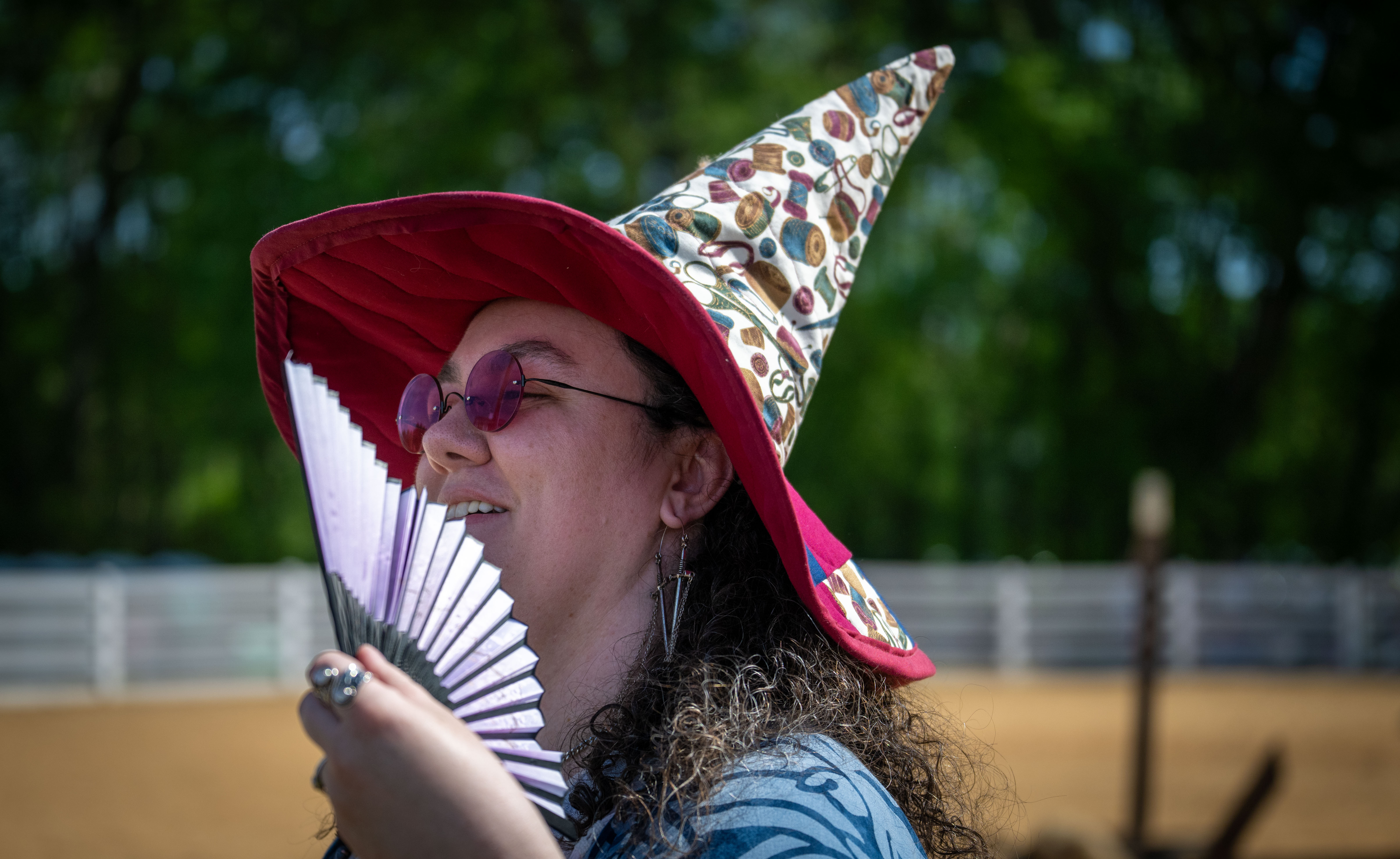 A woman wearing a witch hat fanning herslef with a fan.