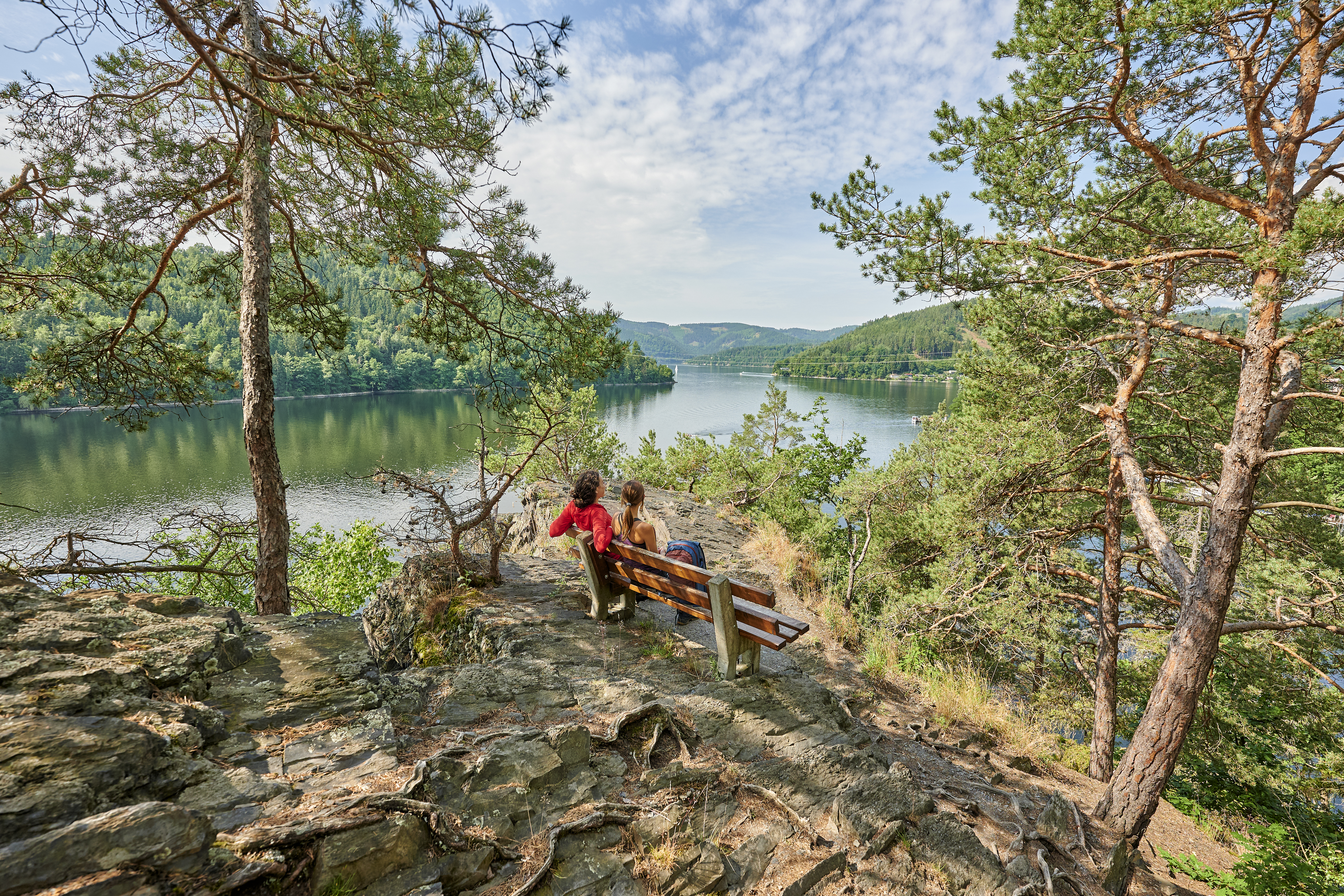 Two people sit on a bench overlooking the Hohenwarte reservoir. The ...