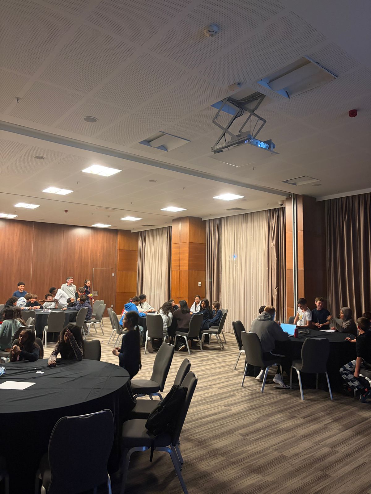 Large, brightly lit room with multiple groups of children seated at ...