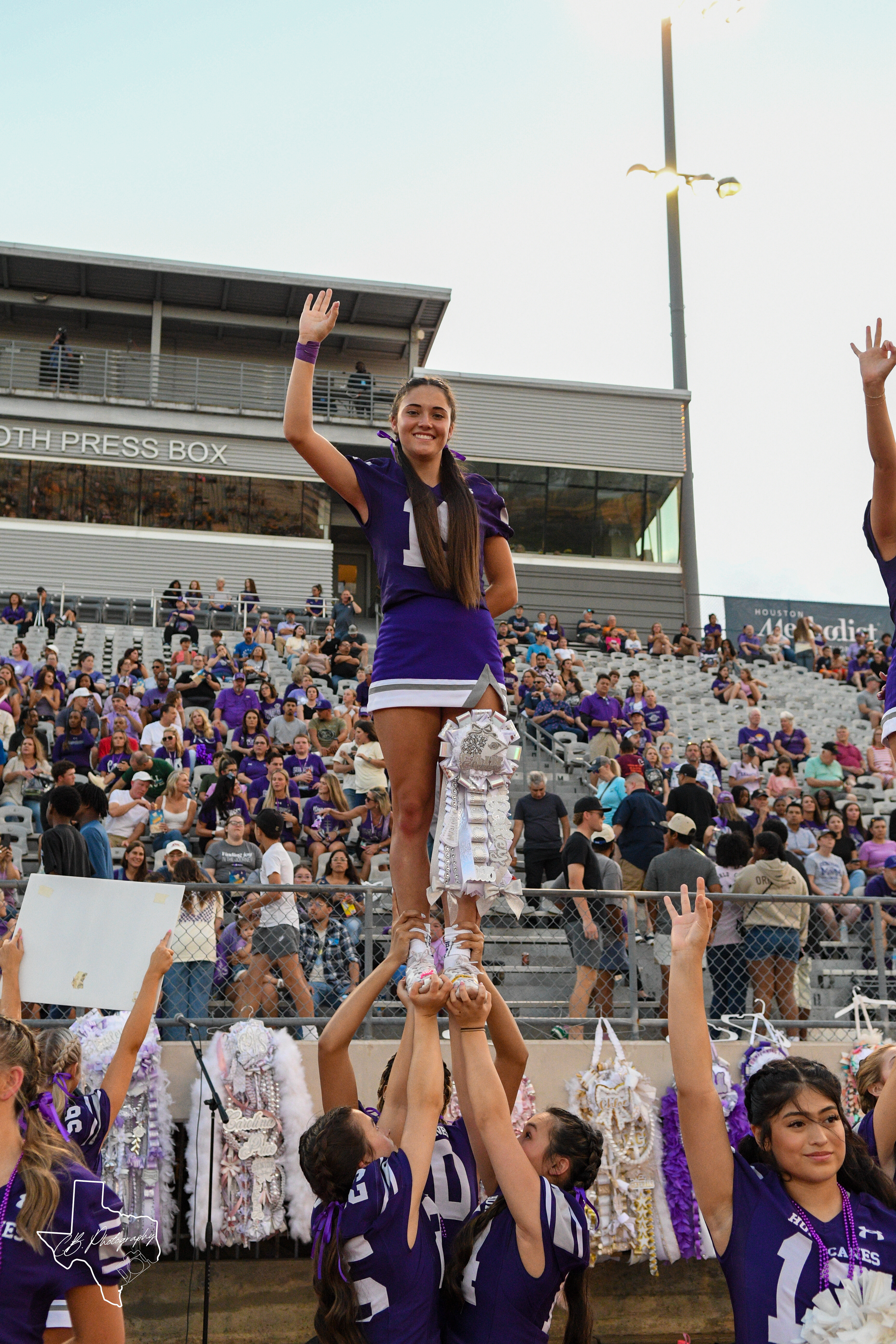 A cheerleader waves while being held up by teammates at a football game ...