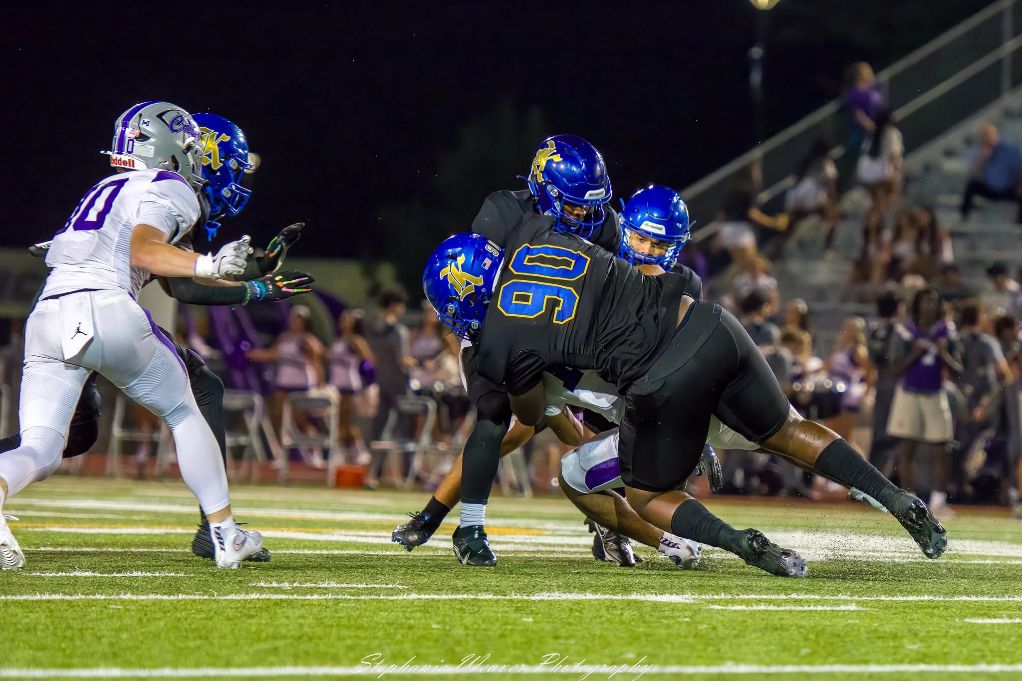 Football players in helmets and pads collide on a green field during a ...