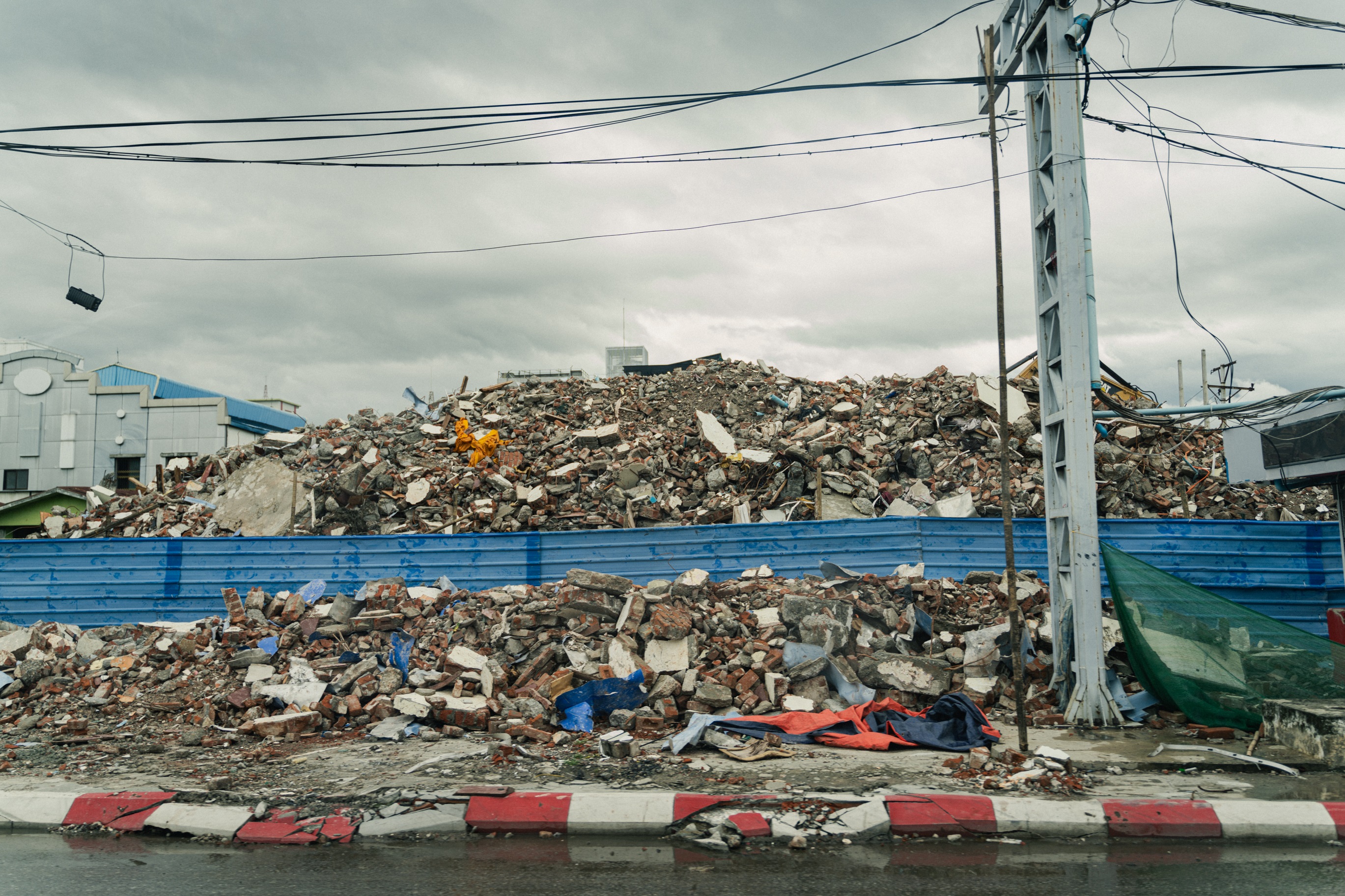 A large pile of rubble and debris sits behind a blue fence under a ...