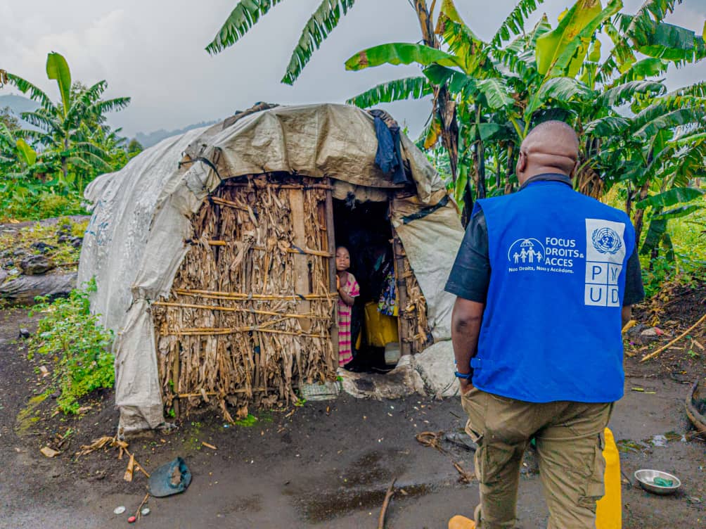 A humanitarian worker stands facing a makeshift shelter where a child ...
