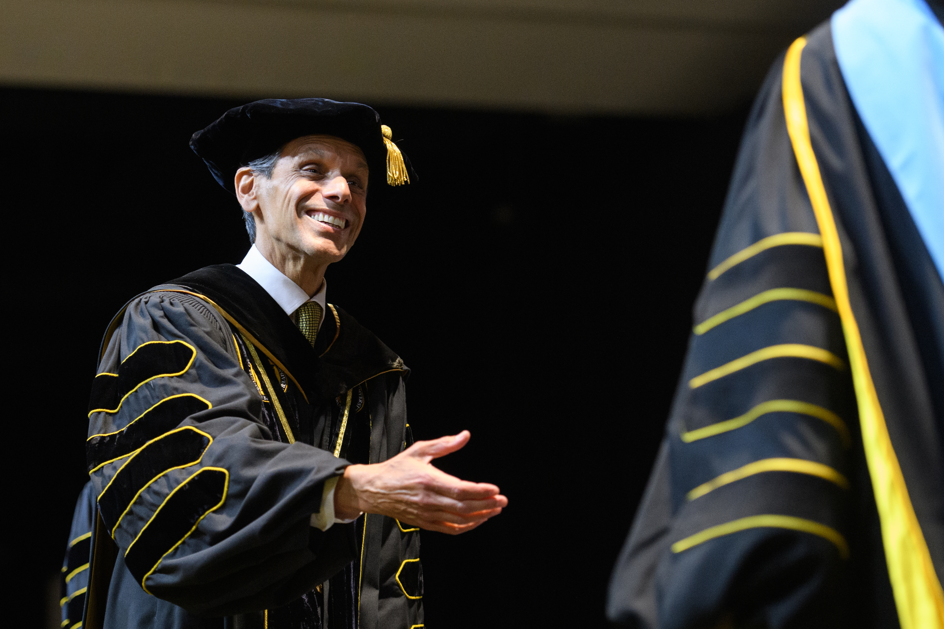 VCU President Michael Rao, in cap and gown, walks toward a graduate ...