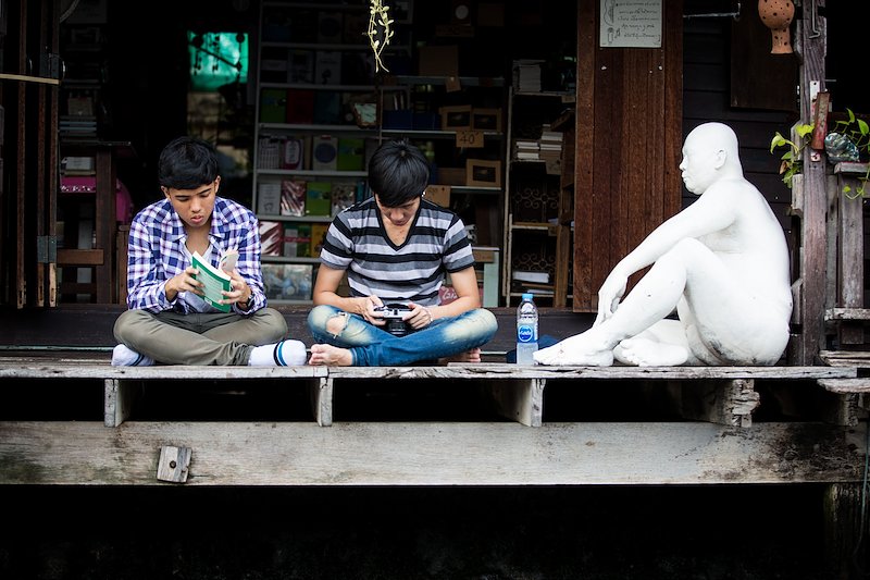 Two Thai art students looking intently at their book and camera alongside a white statue.