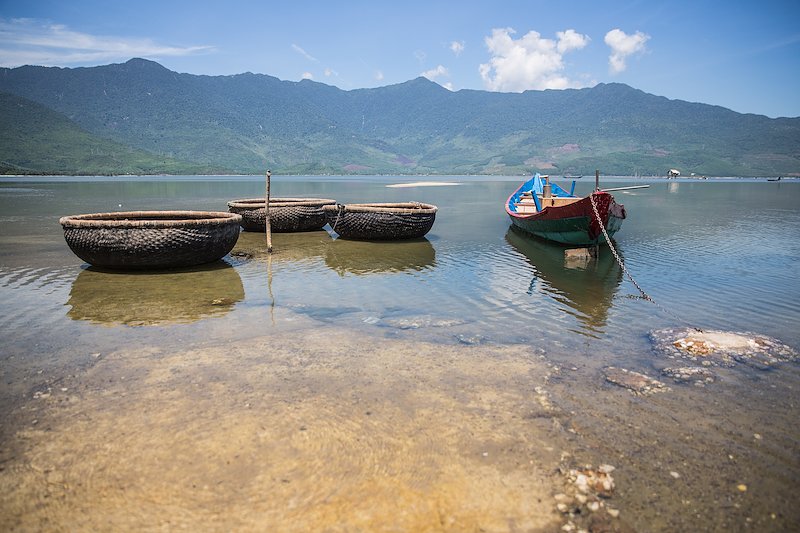 Three traditional woven bamboo boats float alongside a longtail boat.