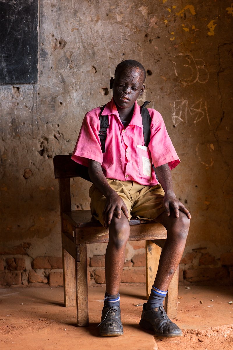 Portrait of Swabil sitting on a wooden chair wearing his school uniform.