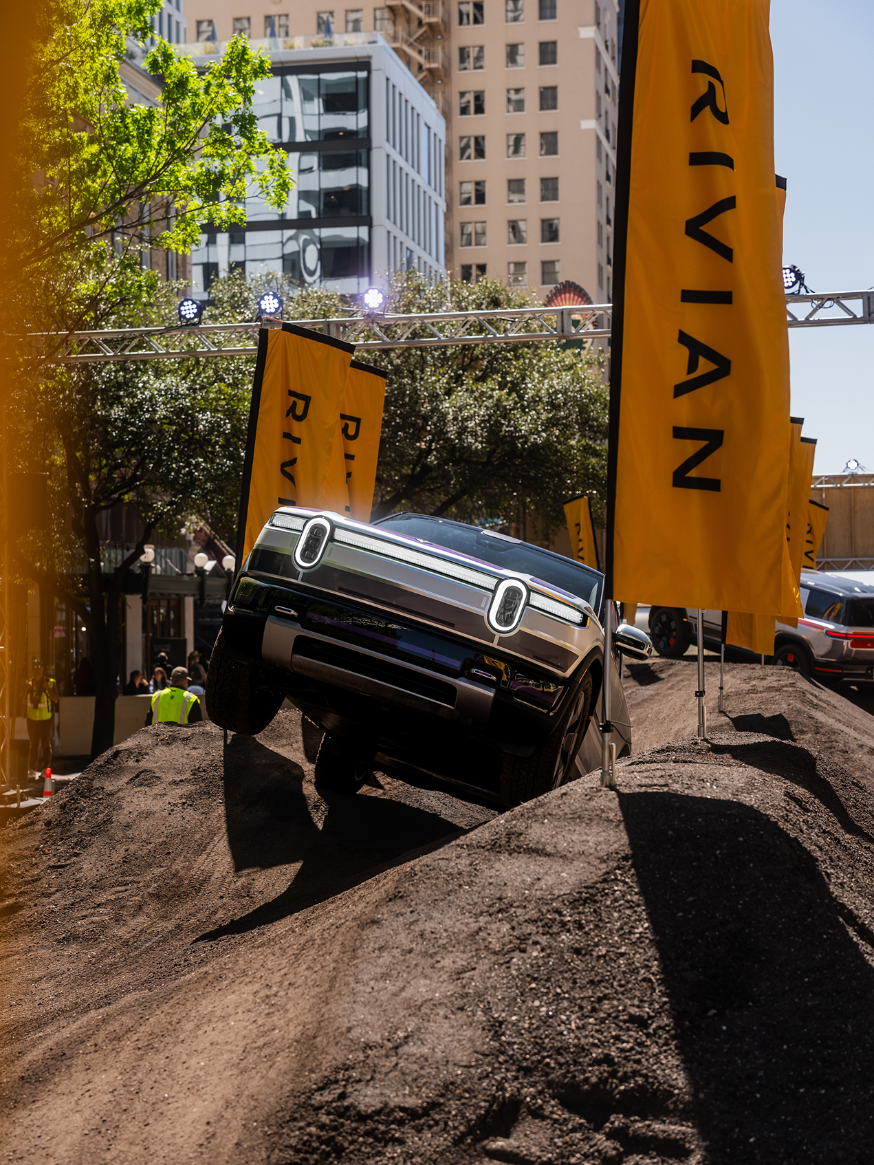 Rivian truck climbs a dirt hill at SXSW 2026. Yellow Rivian flags line ...
