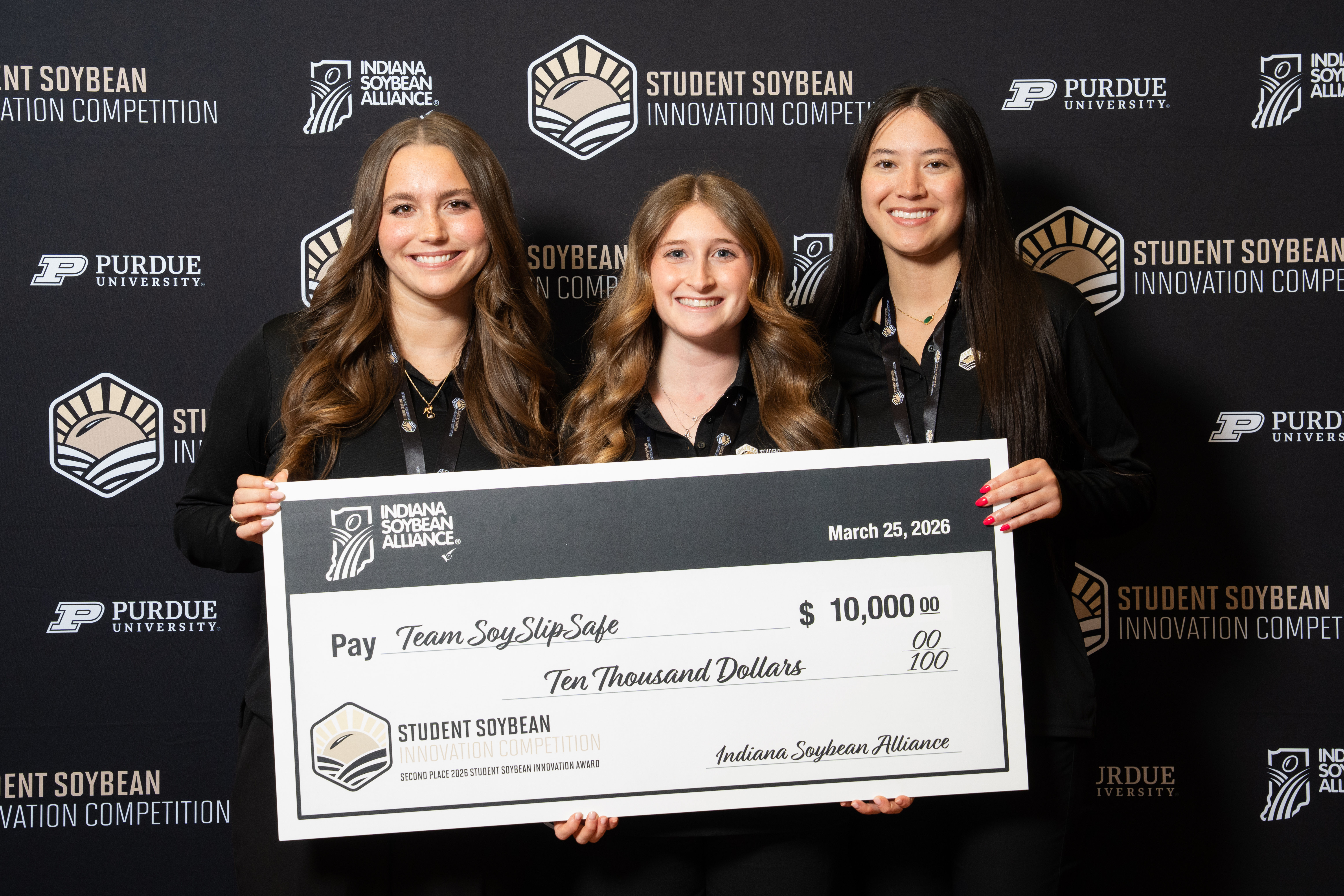 Three smiling women hold a large check for $10,000 made out to