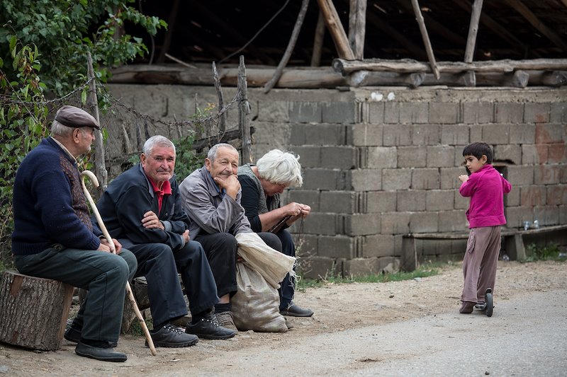 A group of elderly villagers sit along the road. A majority of Razlovci's remaining citizens are elderly.