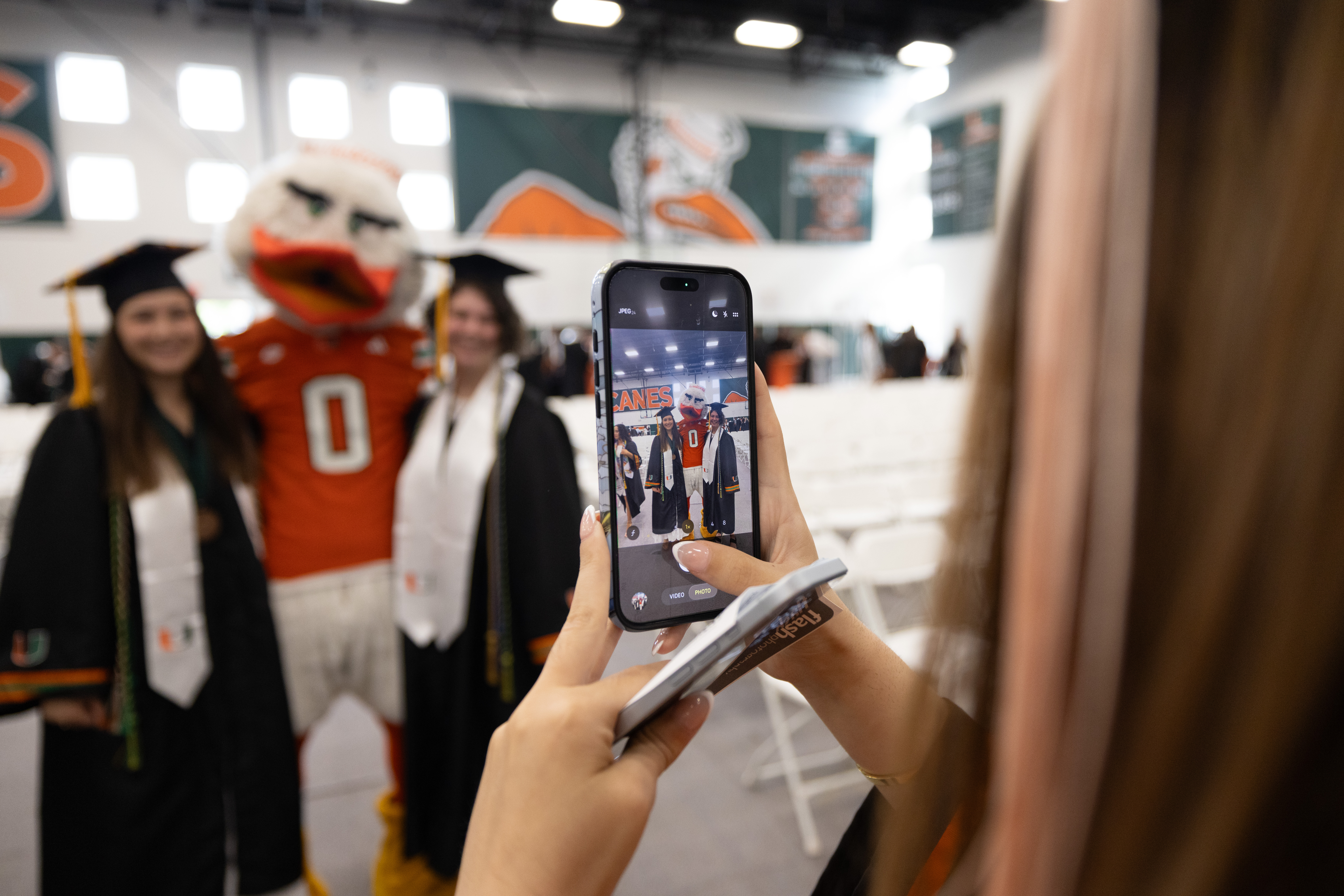 Hands hold phone displaying photo of two graduates and mascot in caps ...