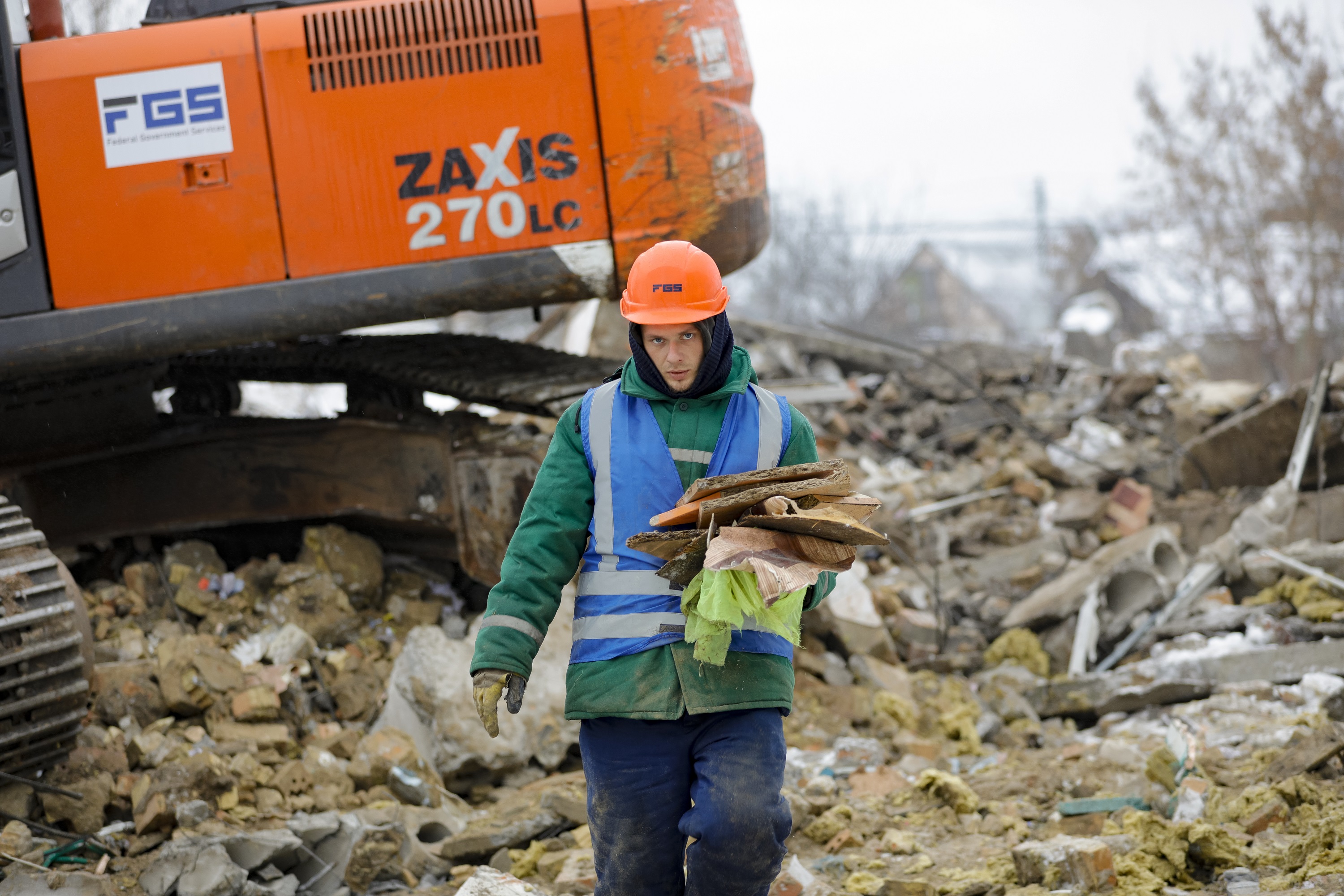 Worker in hardhat carries debris from a demolition site with an orange ...