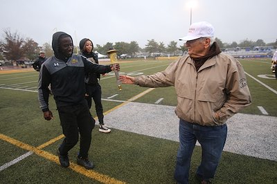 A ceremonial torch passing at halftime of the Rowan-Christopher Newport football game included track-and-field athletes (from left) Nana Agyemang and Jasmine Broadway passing the torch to Oteri...