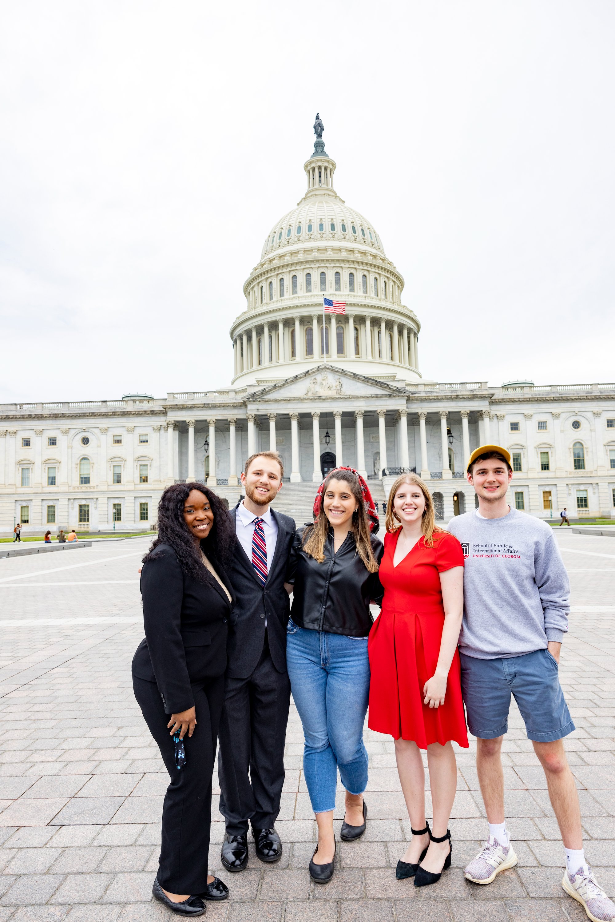 Five UGA students (three female and two male) put their arms around each other and smile toward the camera. Behind them stands the U.S. Capitol.