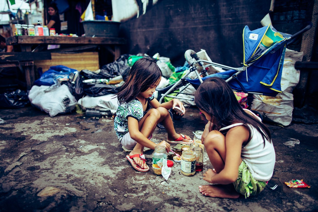 Children make the best of what they have, as these girls enjoy a pretend game of “house” and prepare food in their kitchen.