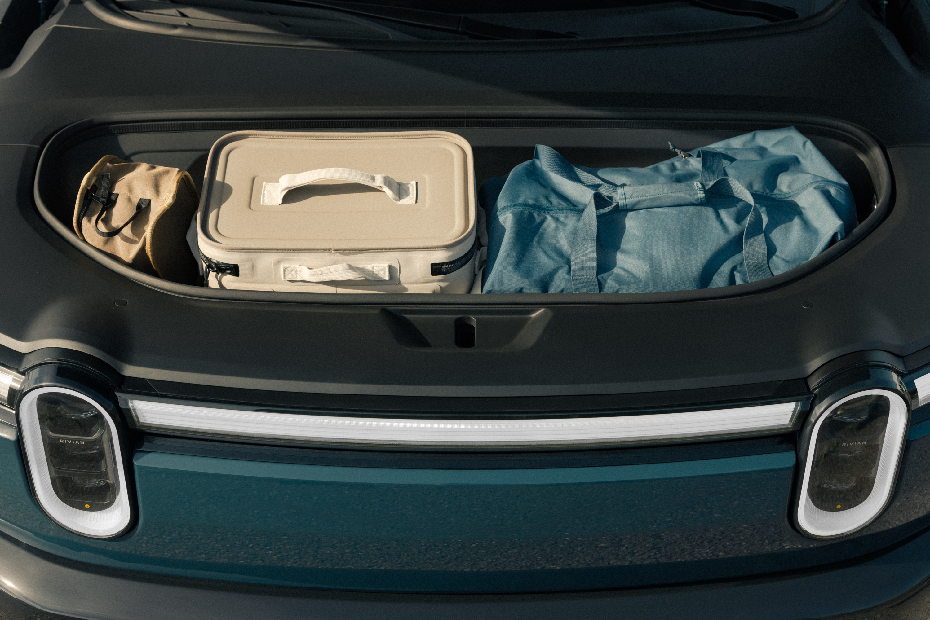 Open front trunk of a Rivian electric truck holds a tan tote bag, a ...