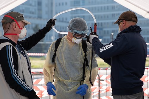 During an infectious disease outbreak, the Water Sanitation and Hygiene (WASH) staff play a critical role alongside the medical staff. WASH team members John, Jeremiah, and Scott help each other gear up for a trip inside the hot zone in Cremona.